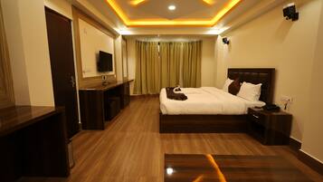 A modern hotel room with a wooden floor, a large bed with white bedding, a desk with a chair, and a television.