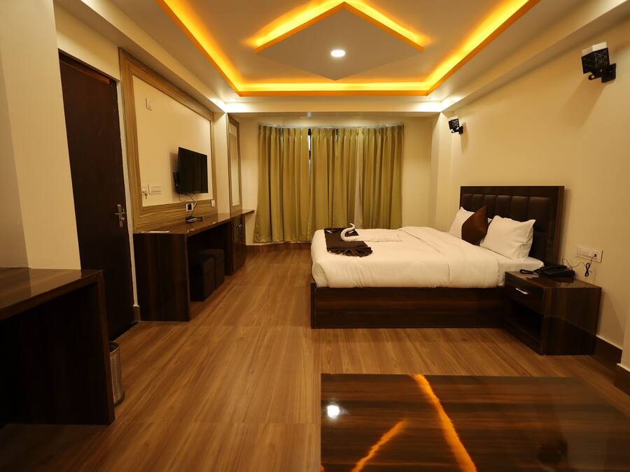 A modern hotel room with a wooden floor, a large bed with white bedding, a desk with a chair, and a television.