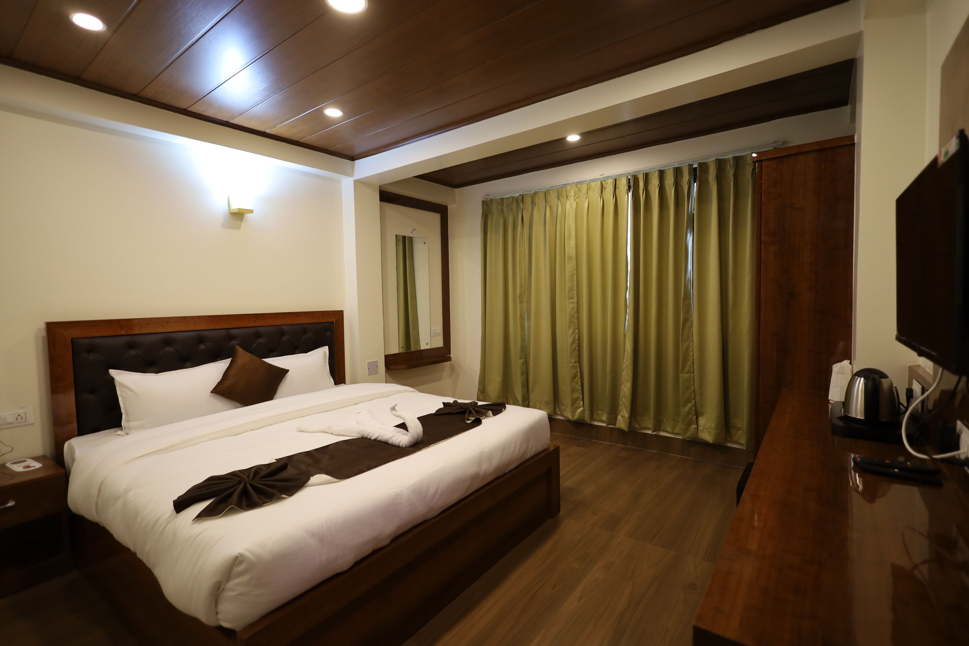 Una habitación de hotel con una cama grande, cabecera de madera y un escritorio de madera con hervidor.