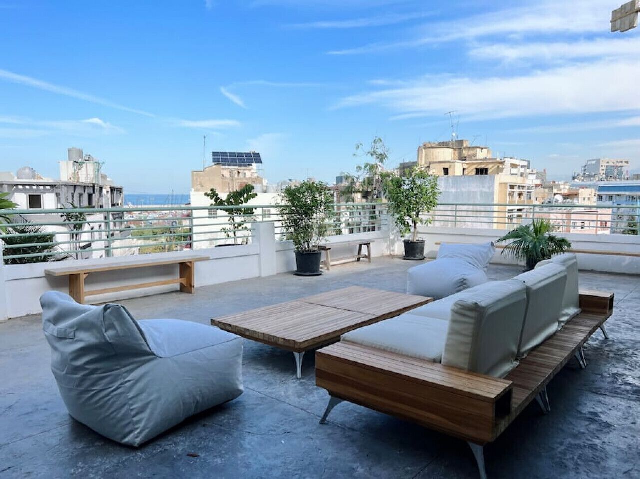 A rooftop terrace with a sofa set, a wooden table, and potted plants.
