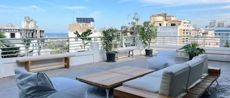 A rooftop terrace with a sofa set, a wooden table, and potted plants.