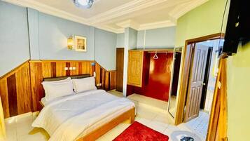 Un dormitorio con cabecera de madera, cama con ropa de cama blanca, alfombra roja y un espejo en la pared.