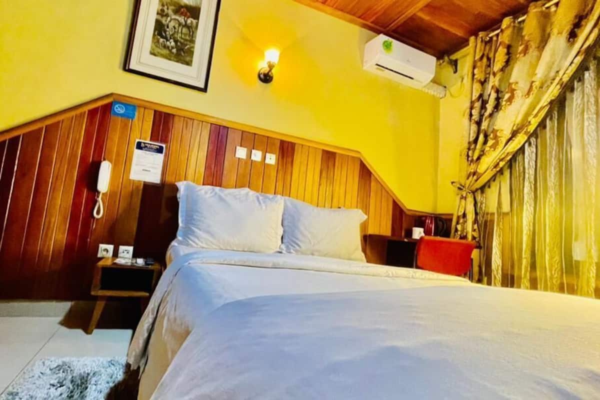 A bedroom with a wooden headboard, a bed with white bedding, a bedside table, a nightstand, and a wall-mounted phone.