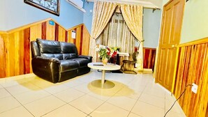 A room with a black leather sofa, a small round table with a vase of flowers, and a wooden wall paneling. - MARVEL HOTEL BUEA (Buea)
