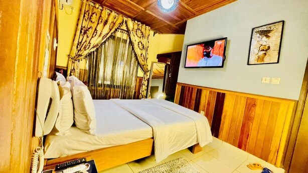 A bedroom with a bed, curtains, a television, and artwork on the wall. - MARVEL HOTEL BUEA (Buea)