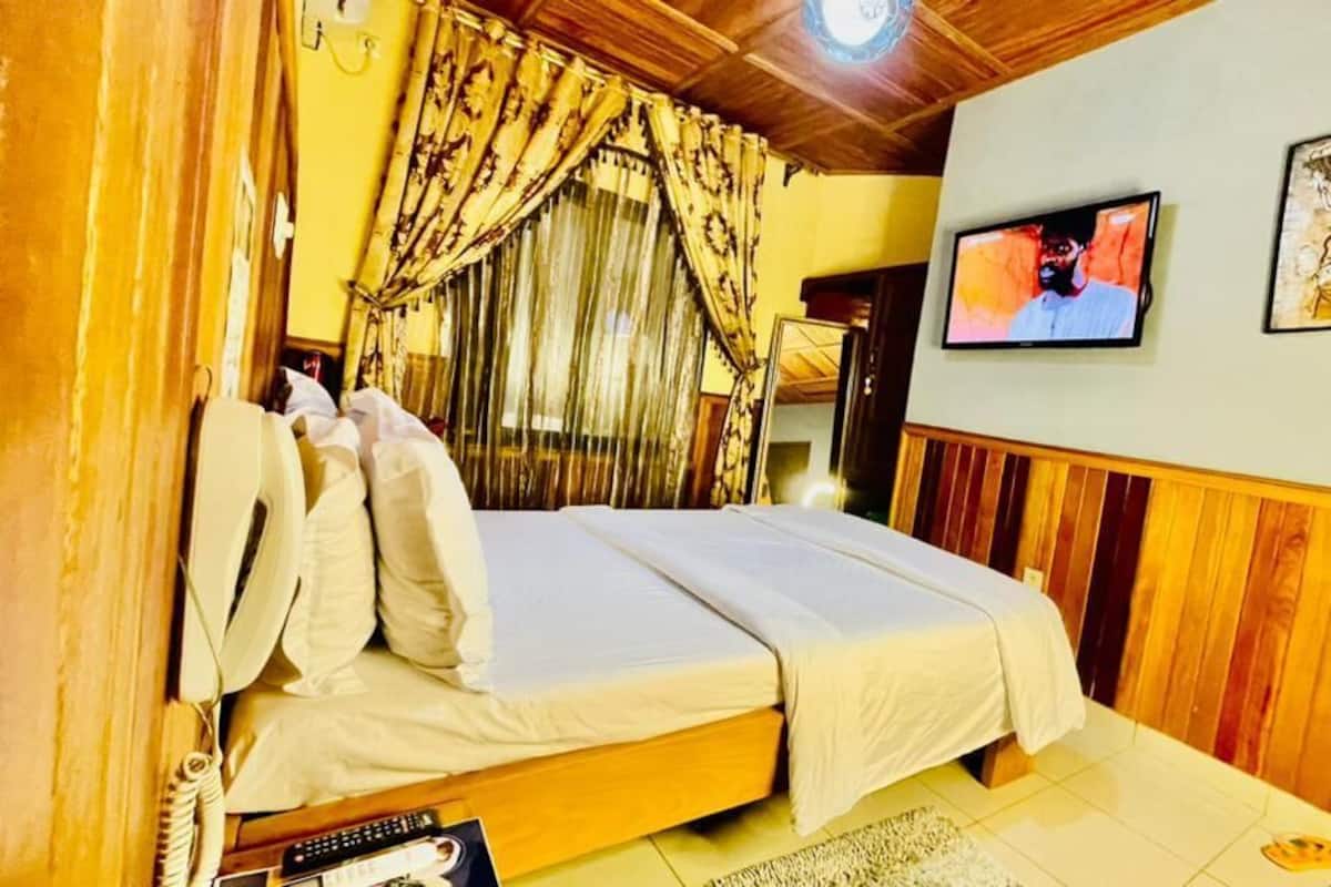 A bedroom with a bed, curtains, a television, and artwork on the wall.