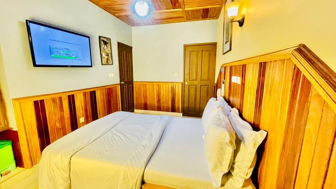 A room with a bed, a television mounted on the wall, and a wooden ceiling.