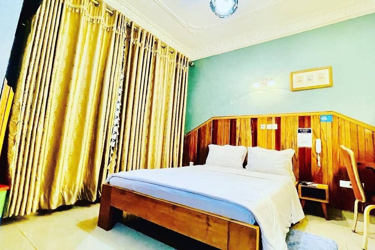 A hotel room with a wooden bed, a nightstand, a chair, and a curtain.