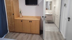 Un dormitorio con un armario de madera, un televisor montado y un baño visible a través de una puerta abierta.