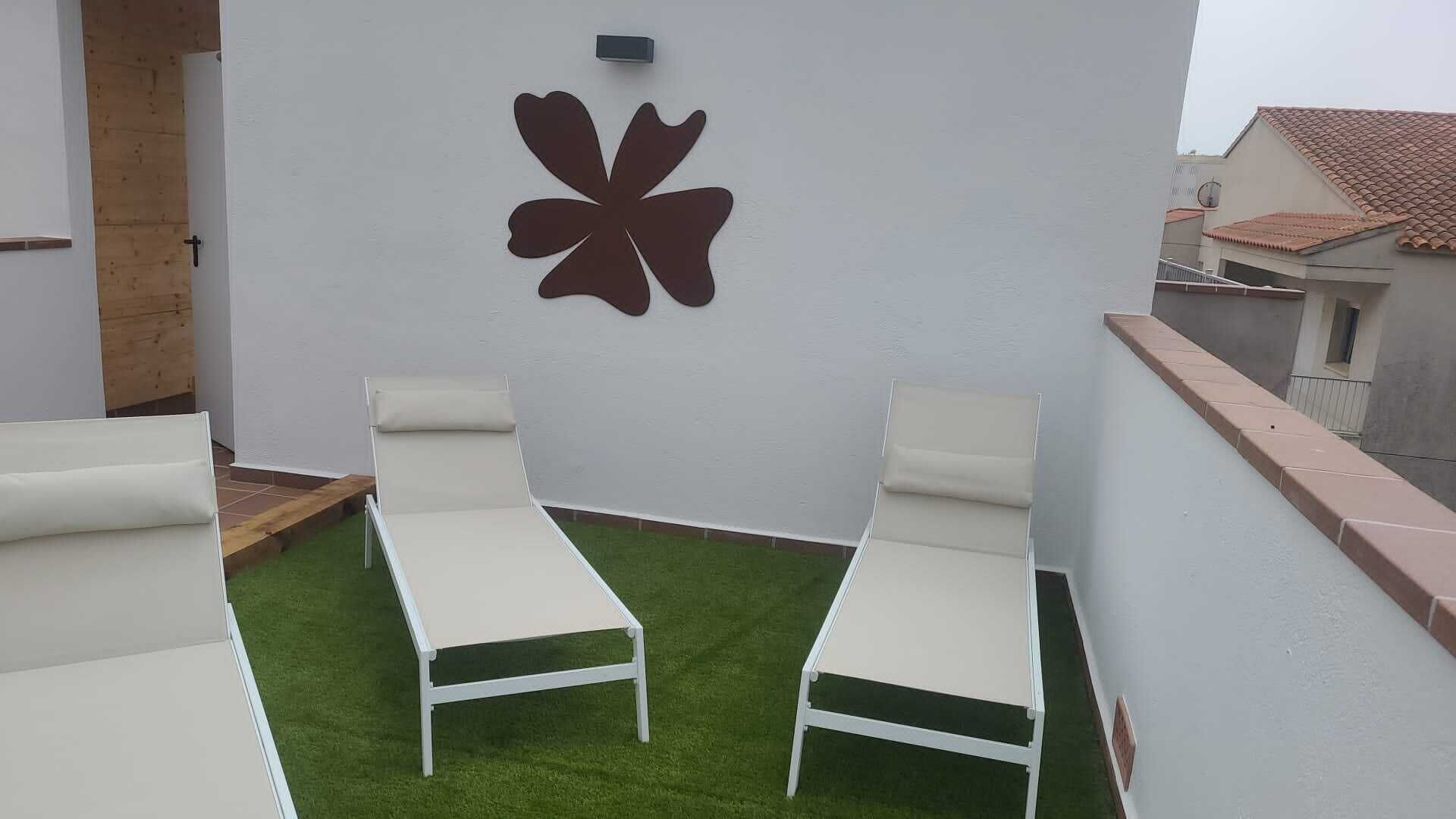 A rooftop terrace with two white lounge chairs, a decorative wall piece, and a small patch of artificial grass.