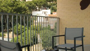 Un balcón con dos sillas y una mesa, con vistas a una zona montañosa con edificios y vegetación.