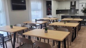 Un comedor con varias mesas y sillas, una cocina con armarios y electrodomésticos, y un televisor montado en la pared.
