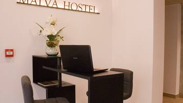 Un espacio de trabajo con una computadora portátil, dos sillas, un florero con flores y un letrero que dice "MAIVA HOSTEL".