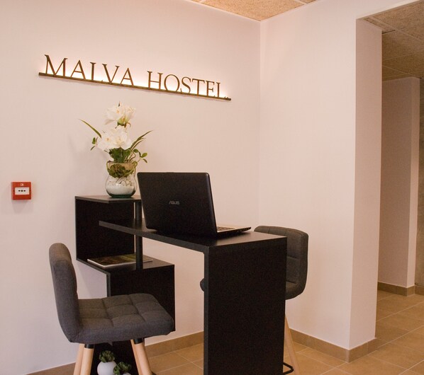 A workspace with a laptop, two chairs, a vase with flowers, and a sign reading "MAIVA HOSTEL". - Malva Inn Estartit (Torroella de Montgrí)