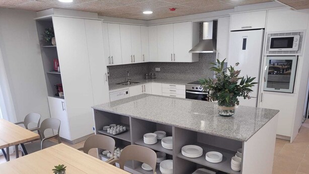 Una cocina moderna con armarios blancos, encimera de granito y horno empotrado. Hay sillas, una mesa y una planta en maceta sobre la encimera.