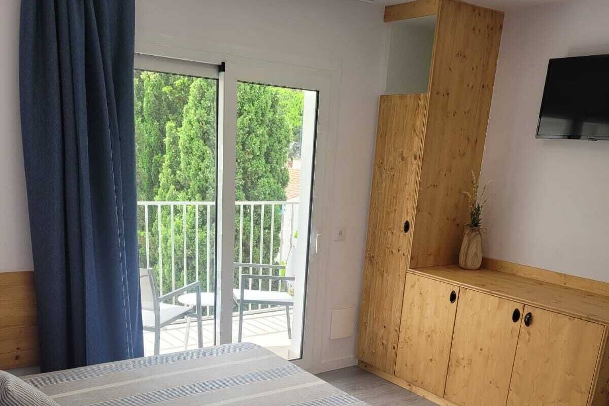 Un dormitorio con cama, un armario de madera, televisor y balcón con vistas a la vegetación.