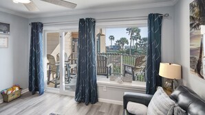 A living room with a view of a deck, a black leather sofa, a lamp, and a rug. - Monthly Discount! Ocean View Heated Pool Hot tub! (Galveston)