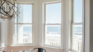 Een eetgedeelte met een tafel gedekt voor twee personen, grote ramen met uitzicht op de oceaan en een opvallende, sferische lamp.