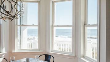 A dining area with a table set for two, large windows with a view of the ocean, and a unique spherical light fixture.