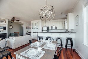A modern kitchen with white cabinets, a stainless steel refrigerator, and a dining area set for four with a wooden table and white placemats.