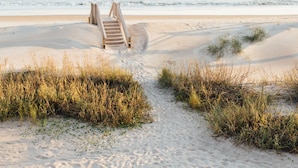 Een zandstrand met een houten trap die naar een hoger gelegen deel leidt.