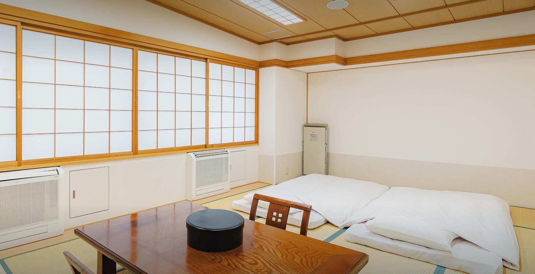 A traditional Japanese room with tatami flooring, a futon bed, a wooden table with a black container, and sliding doors with a grid pattern.