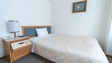 A hotel room with a bed, bedside table, lamp, and a clock on the wall.
