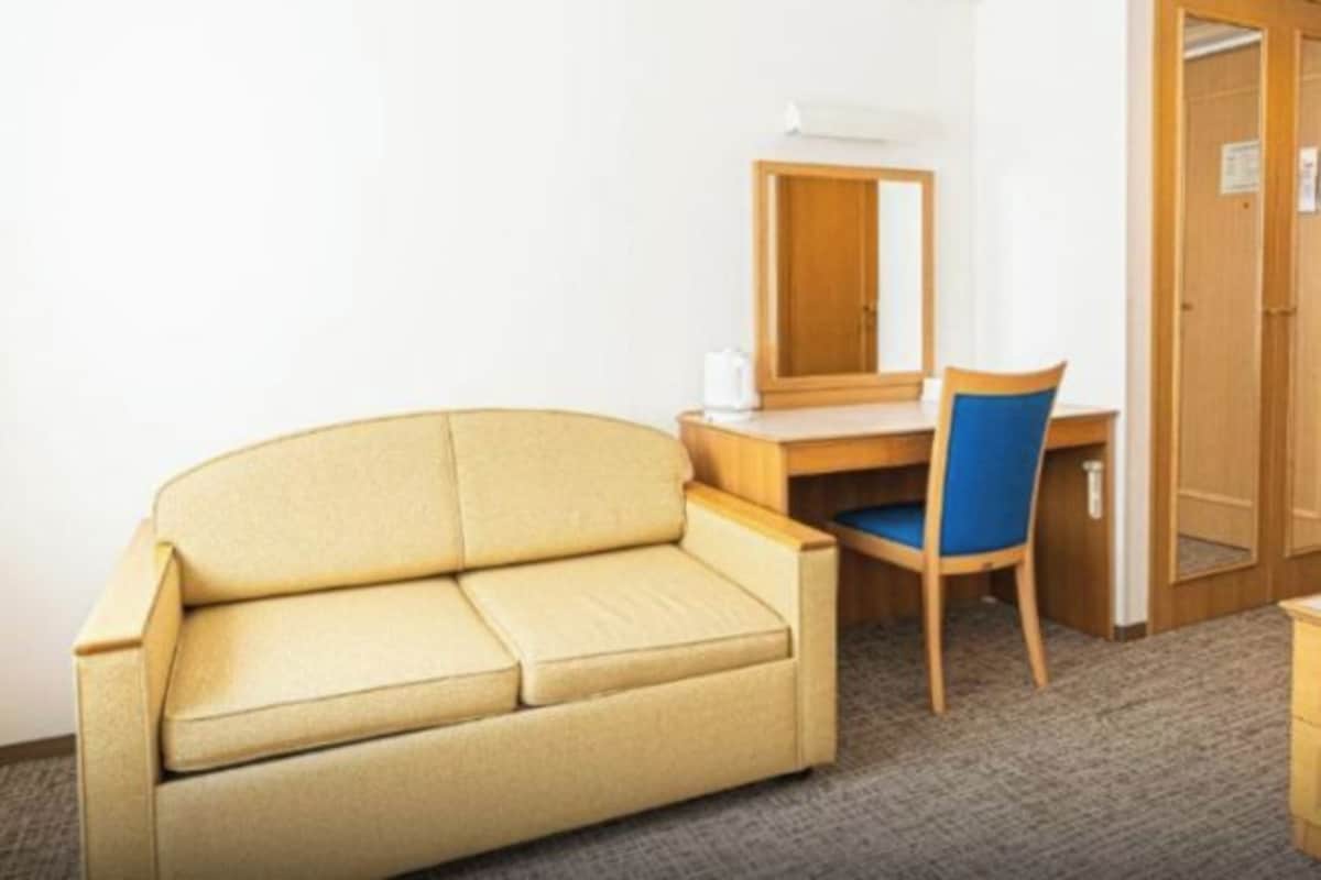 Una habitación con un sofá color crema, un escritorio de madera con una silla, y un armario de madera.