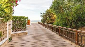 Een houten looppad dat naar een strand leidt, omzoomd door groen en een hek.