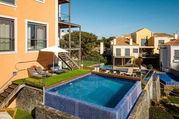 A swimming pool with a tiled edge, surrounded by lounge chairs and a staircase leading to an upper level. - Vale Lobo Golf & Beach with Private Pool I (Vale do Lobo)