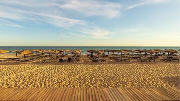 A beach with wooden deck chairs and umbrellas, a sandy beach, and the ocean in the background.