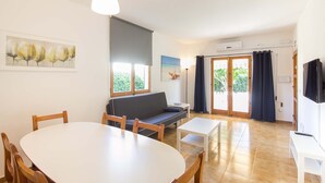 Una habitación con una mesa de comedor redonda, un sofá, un televisor y una ventana con cortinas.
