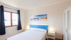Un dormitorio con una cama, dos mesitas de noche, una ventana con cortinas e imagen colgada en la pared.