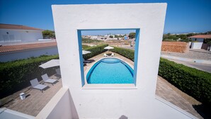 Una piscina con dos sillas de descanso y una mesita, rodeada por un muro blanco y un cielo azul despejado.