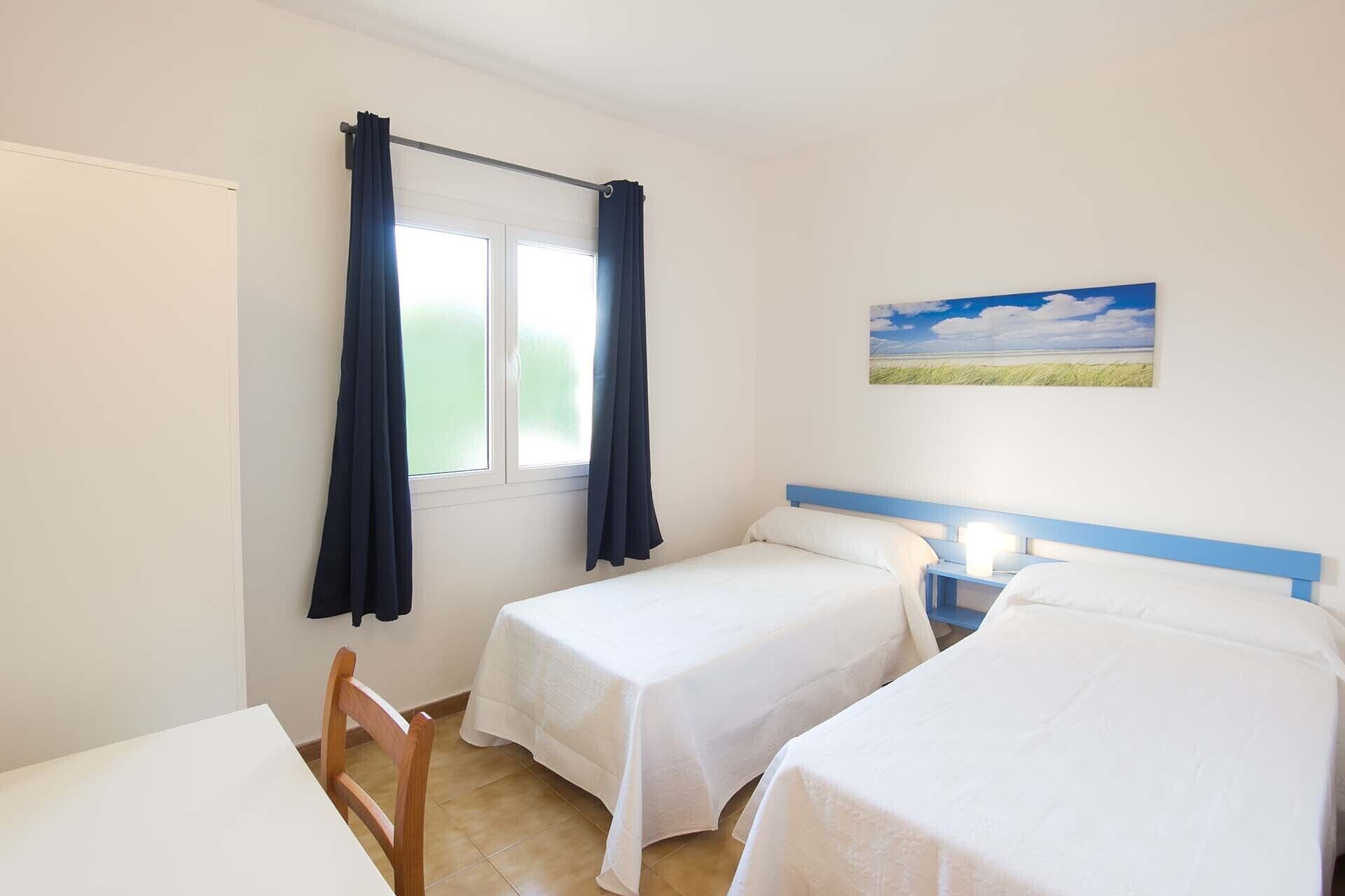 Una habitación con dos camas individuales, una ventana con cortinas, un cuadro en la pared y una silla.