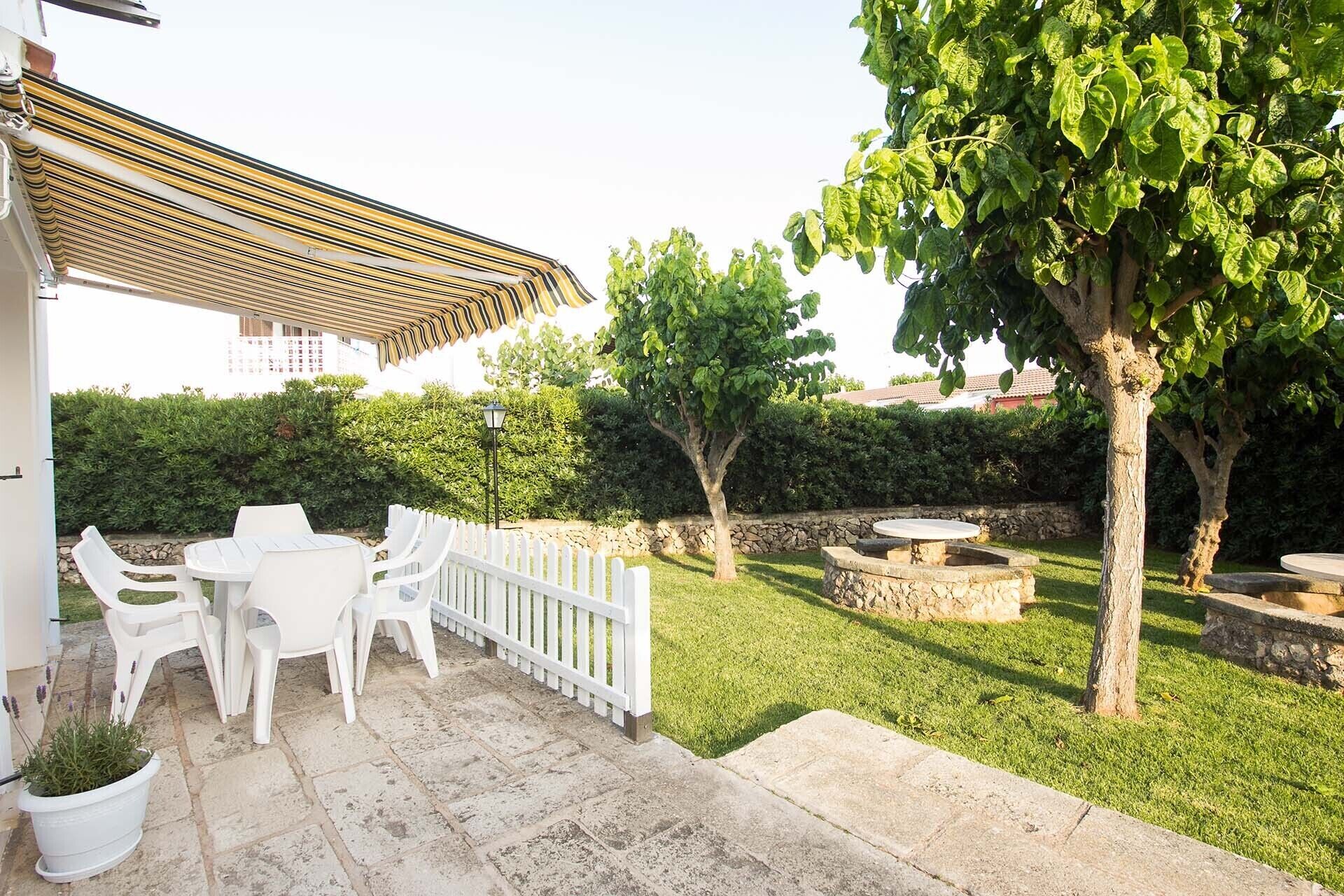 A patio area with white plastic chairs and a table, a stone pathway, and a small tree.