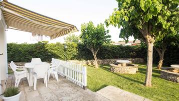 A patio area with white plastic chairs and a table, a stone pathway, and a small tree.
