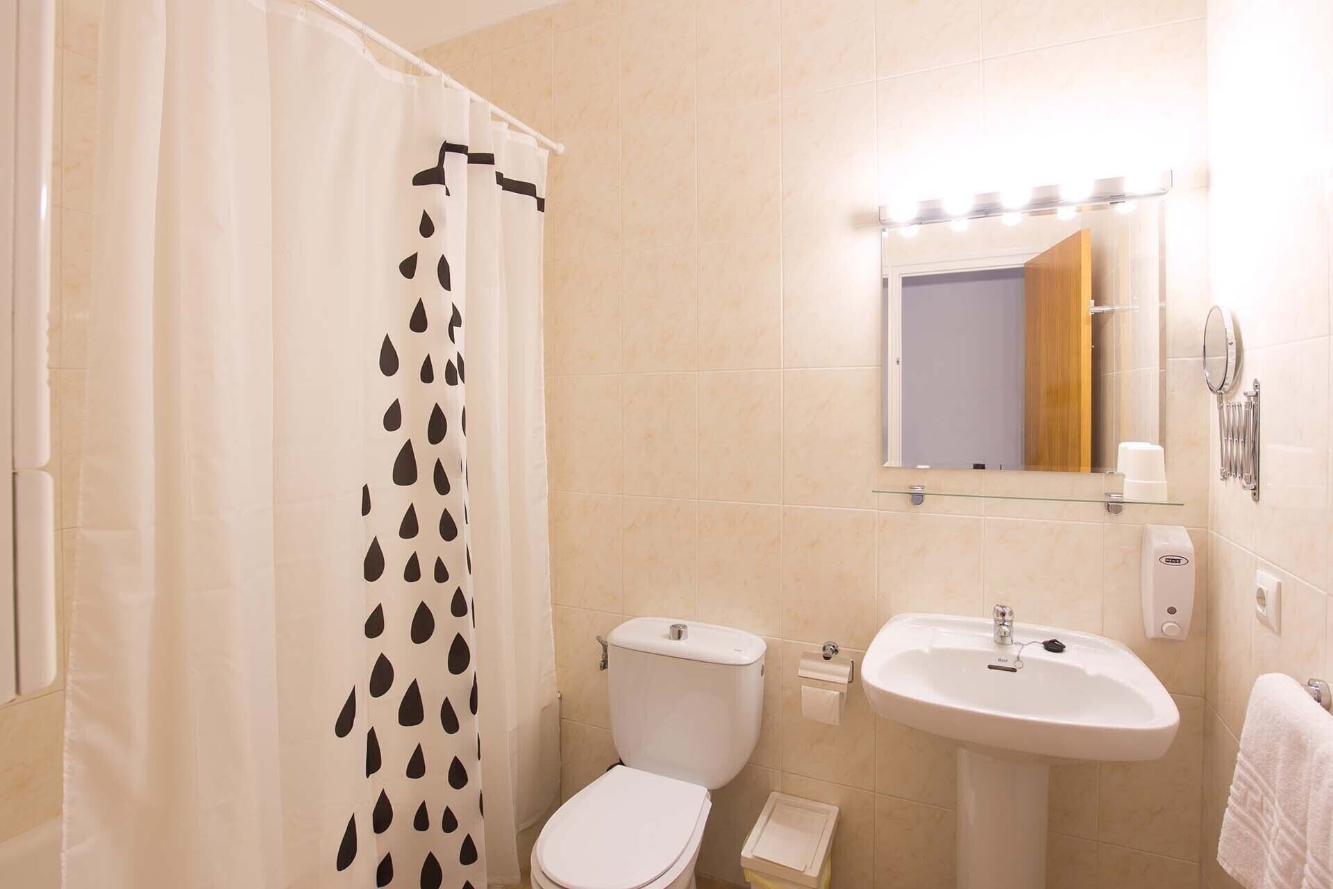 Un baño con cortina de ducha, inodoro, lavamanos y espejo.