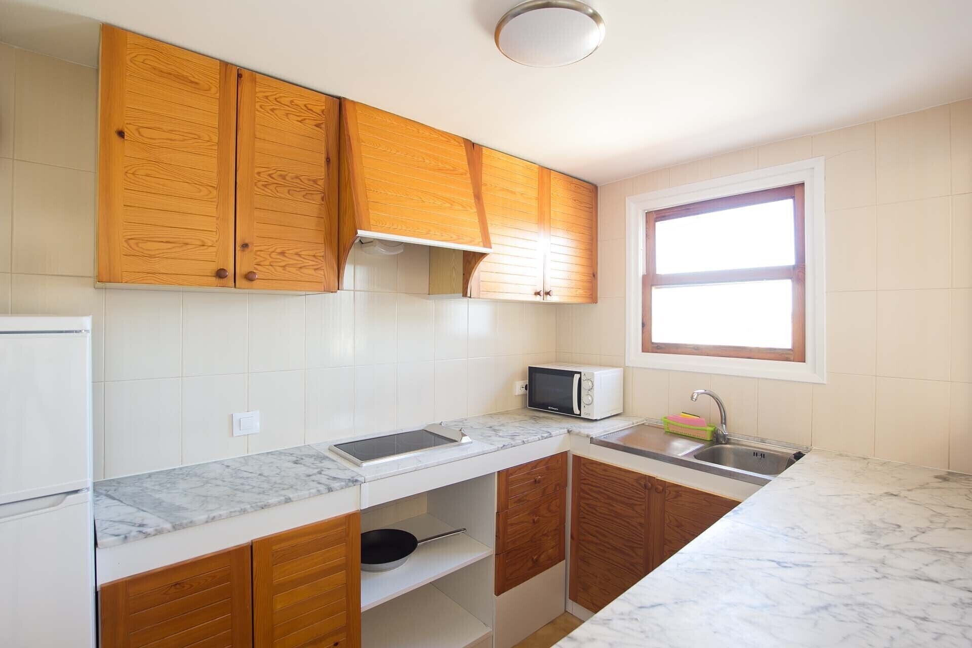 Una cocina con armarios de madera, microondas, fregadero y ventana.