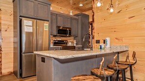 A modern kitchen with stainless steel appliances, granite countertops, and wooden bar stools. - 🏔️Rustic Mountain View🌲Resort Pool, Hot Tub & Game Room (Sevierville)