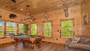 A wooden cabin interior with a pool table, a couch, and deer heads mounted on the ceiling. - 🏔️Rustic Mountain View🌲Resort Pool, Hot Tub & Game Room (Sevierville)