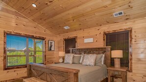 A wooden cabin bedroom with a bed, bench, bedside tables, and a view of the outdoors. - 🏔️Rustic Mountain View🌲Resort Pool, Hot Tub & Game Room (Sevierville)