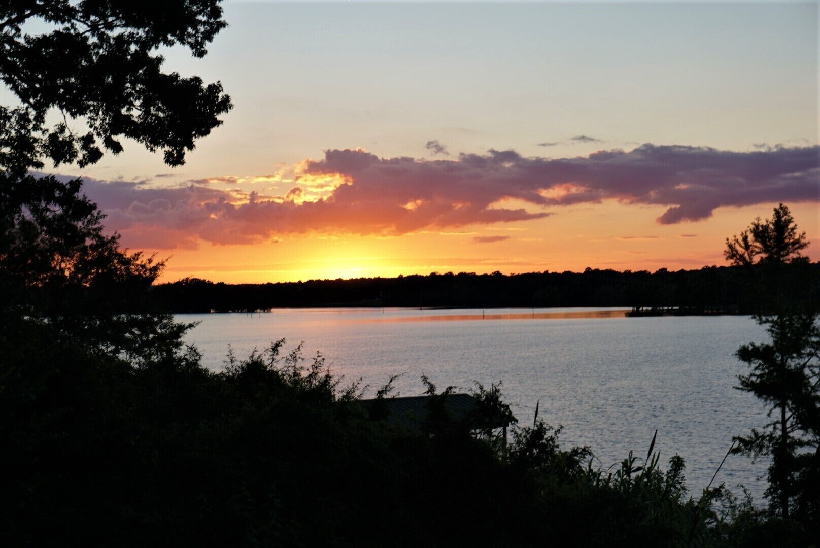 A sunset over a calm lake with trees in the foreground.