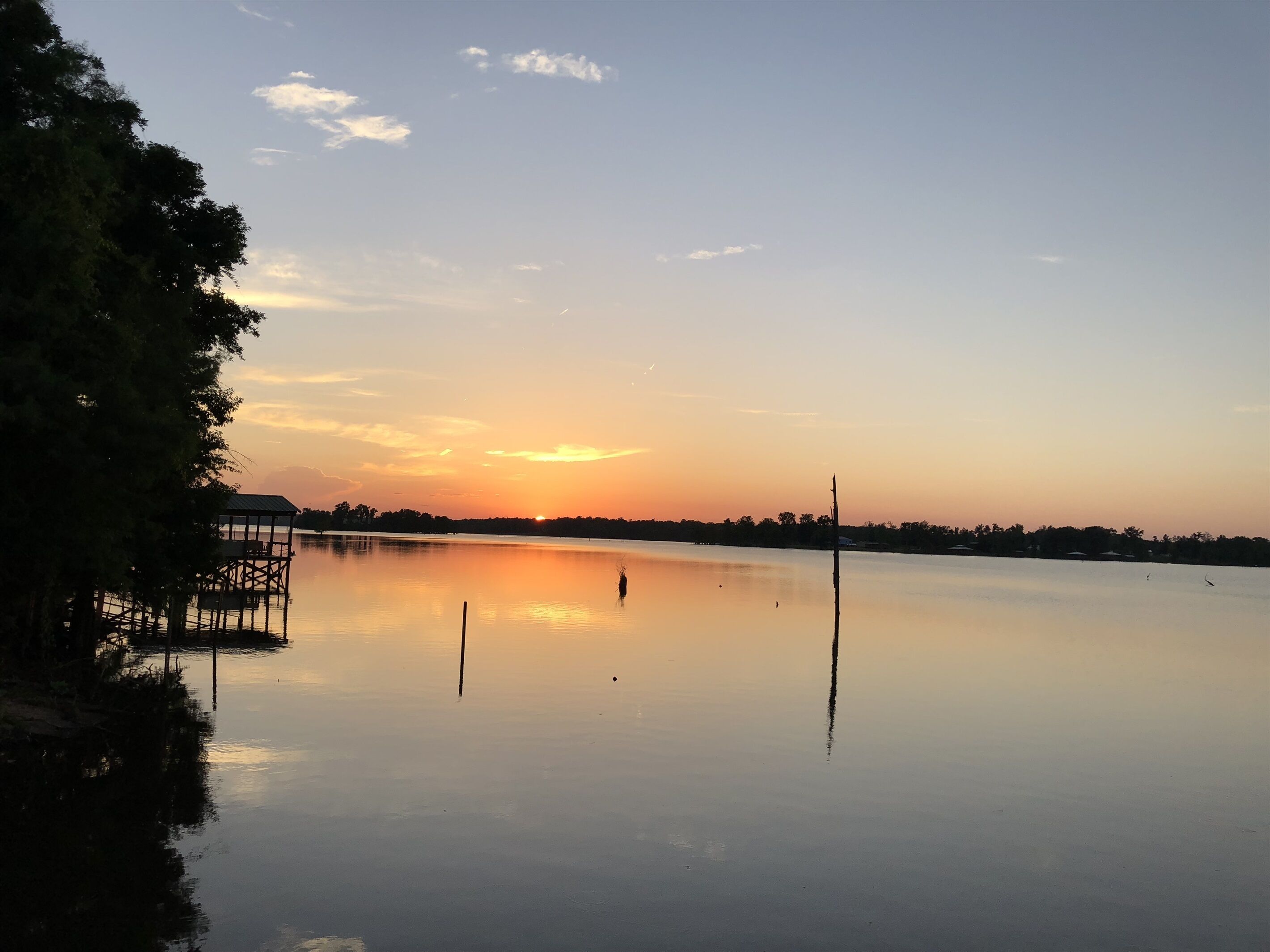 Un lago tranquilo al atardecer con un muelle y árboles.