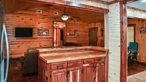 Interior d'una cabana de fusta amb zona de cuina que inclou un taulell i armaris de fusta, un ventilador de sostre i un cartell amb la frase "Welcome to the Lake".