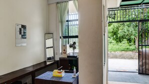 Una habitación con una mesa, una ventana con cortinas, un ventilador y una puerta que da al exterior.