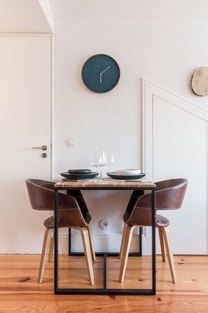 Un coin repas avec une table dressée pour deux personnes, deux fauteuils en cuir, une horloge murale ronde de couleur sombre et un plancher en bois.