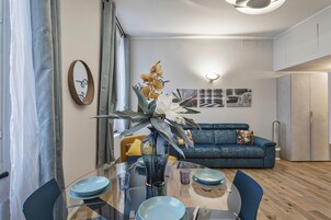 Una sala moderna con una mesa de comedor de vidrio, sofá azul y una planta decorativa.