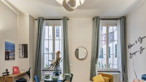A modern living room with a dining area, large windows with curtains, a round mirror, and a welcome sign.