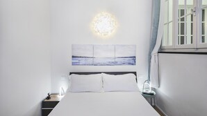 A bedroom with a bed, a wall-mounted light, a painting, and a window with curtains.